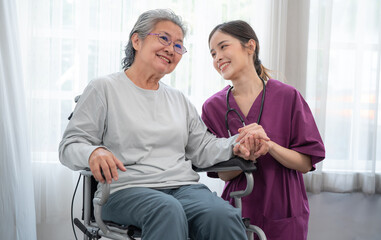 Asian young nurse taking care and talking mature female patient sitting on wheelchair in hospital. Healthcare concept.