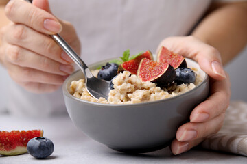 Woman holding bowl of oatmeal with blueberries and fig pieces at white table, closeup