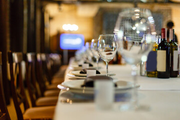 Close up new white porcelain tableware plates on purple place mats and empty wine glasses ready for dinner. Table settings wait for guests at home or restaurant.
