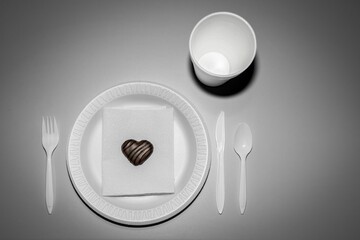 Grayscale top view of a plastic plate with a chocolate candy, a cup, and plastic cutlery