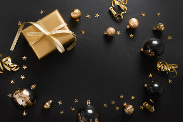 Shiny black balls and golden gift with on black background. Happy New Year. View from above. Copy space.