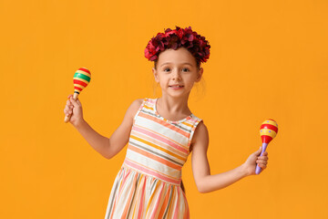 Little Mexican girl with floral wreath and maracas on yellow background
