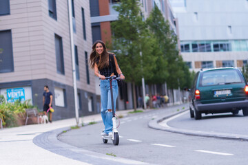 Fototapeta na wymiar A young brunette woman moving in the city with an electric scooter smiling, along the bike path