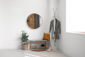 Interior of stylish hall with round mirror, bench and rack
