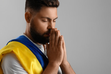 Young man with flag of Ukraine praying on grey background, closeup