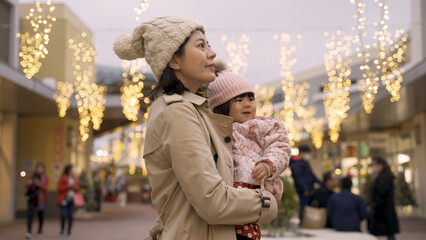 smiling asian mother and baby turning and looking around at beautiful outdoor Christmas lights...