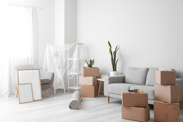 Cardboard boxes with sofa, armchair, frames and shelving unit in living room on moving day