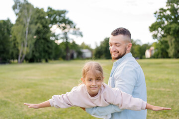 Fototapeta premium Playful handsome bearded Caucasian father having fun with his adorable daughter in park.