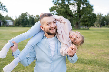Fototapeta premium Cute and happy little girl spending time with her young loving father while visiting park , they have fun together.