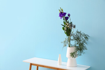 Vases with beautiful ikebana on table near blue wall