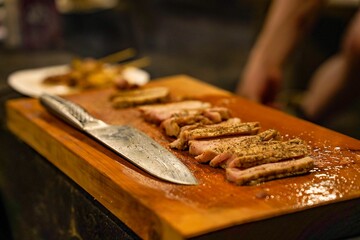 Closeup shot of a wooden board with sliced barbecued pork and a silver knife