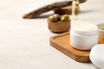Wooden board with jar of natural olive cream on light table, closeup