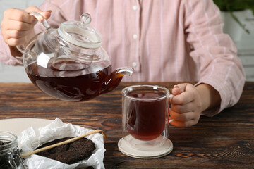 Woman with glass pot and cup of puer tea at wooden table, closeup
