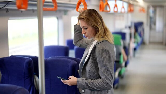 beautiful blonde woman is riding train in underground or suburban railway, standing and using phone