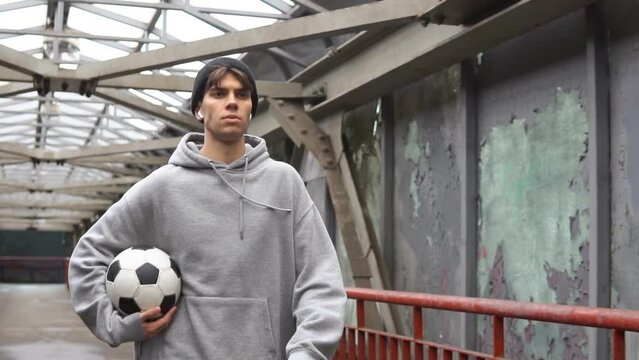 Portrait of a young hipster man street football player with a soccer ball walking on urban background.