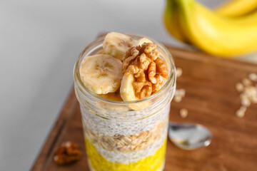 Glass jar of tasty chia seed pudding and banana on white background, closeup