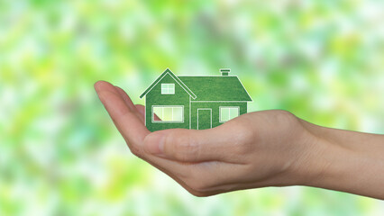 In the palm of a woman's hand, an eco-green house. Blurry green leaves in the background