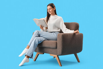 Fototapeta na wymiar Beautiful woman reading book in armchair on blue background