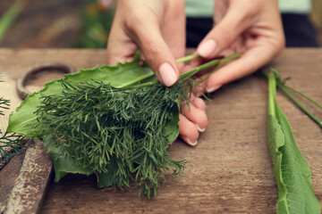 Woman with fresh green herbs at wooden table, closeup