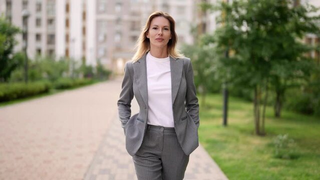 good-looking adult woman in business suit walking in city in summer sunny day or morning, portrait