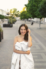 Beautiful young woman wrapped in a white blanket on an empty city road in the morning at dawn.