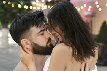 A man and a woman in white blankets hug and kiss in the morning sun on the street.