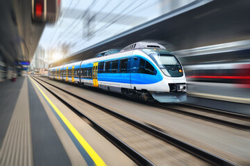 Fototapeta na wymiar High speed train in motion on the train station at sunset. Blue modern intercity passenger train with motion blur effect. Railway platform. Railroad in Europe. Commercial transportation. Concept