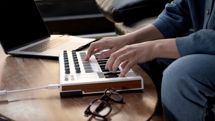 Woman hands playing on small midi controller, producer of music with laptop on table. Closeup of hands playing on keys, home studio with professional equipment. 