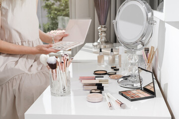 Make-up table, decorative cosmetics for professional and home makeup. Close-up view of brushes, eyeshadow palates in white sunny salon. Beauty Artists hands choosing color of base. Copy space