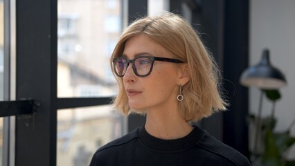 Boss woman in eyeglasses, attractive blonde manager profile portrait thinking and looking out the window. Office room and worker in black clothes. Concept of business partner.  © diproduction