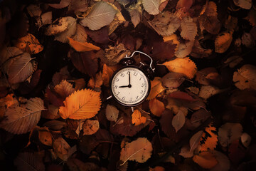 Black alarm clock on colorful maple leaves background. Closeup. Time change concept.