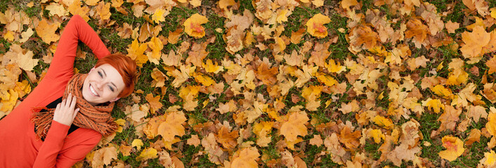 Ginger hair woman lying on autumn leaves, copy space