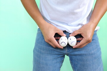 Young Asian man holding two chicken eggs with sad face on crotch groin area. Male infertility, testicular cancer and impotence concept.  © sulit.photos