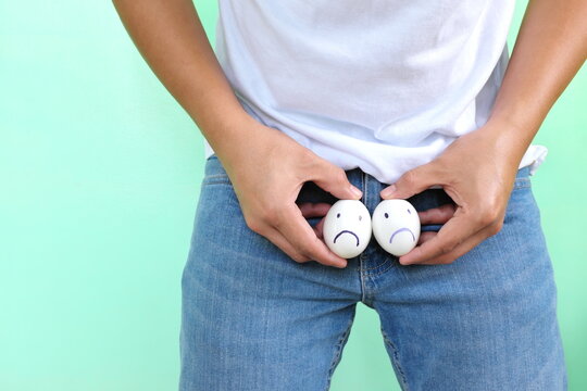 Young Asian man holding two chicken eggs with sad face on crotch groin area. Male infertility, testicular cancer and impotence concept. 
