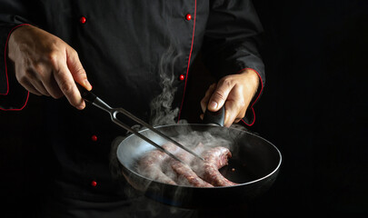 The cook fries meat sausages in a frying pan. Place for hotel menu or recipe on black background