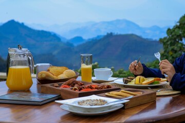 Hands eating a luxury brunch meal on the table, meat, juice and fruits with landscape in background