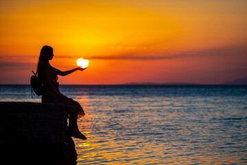 dark silhouette of a long-haired woman in a dress catching the setting sun; spectacular colourful sunset over the adriatic in croatia, peljesac peninsula