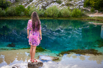 beautiful girl in a dress stands by the mysterious source of the river cetina, in which the clouds are reflected; vacation in croatia