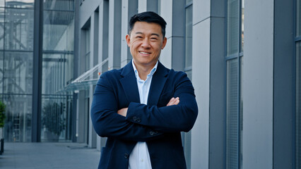 Smiling happy confident motivated successful 40s middle-aged Asian Korean man entrepreneur employer company CEO realtor businessman boss leader posing in downtown outdoors in city crossing hands smile