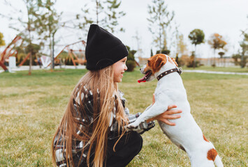 a little girl kisses and hugs her Jack Russell terrier dog in the park. Love between the owner and the dog. a child is holding a dog in his arms.