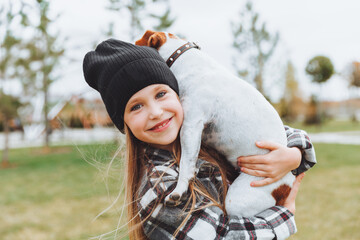 a little girl kisses and hugs her Jack Russell terrier dog in the park. Love between the owner and the dog. a child is holding a dog in his arms.