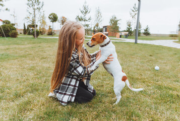 a little girl kisses and hugs her Jack Russell terrier dog in the park. Love between the owner and the dog. a child is holding a dog in his arms.