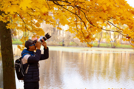 Asian man tourist  hold in hands take photography click on modern photo camera, photographer look on camera in Autumn trees fall season in the park