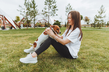 A woman in a white T-shirt and jeans hugs her Jack Russell Terrier dog in nature in the park. Loyal...