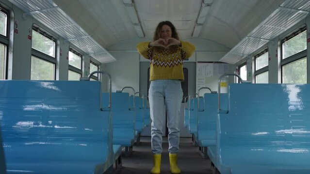 Happy woman puts hands into heart shape standing in train