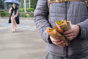 Shawarma takeaway. Roasted meat with vegetables and sauce, shaved for serving in sandwiches. Fast food for lunch. Hand is holding fresh delicious two meats in pita bread.