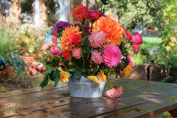 Flowers: roses, asters, dahilia in the apple garden on a wooden table. Floristic design. Sunny day