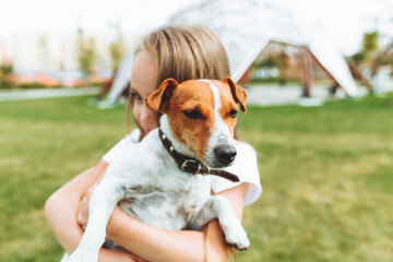 a little girl kisses and hugs her Jack Russell terrier dog in the park. Love between the owner and the dog. a child is holding a dog in his arms.