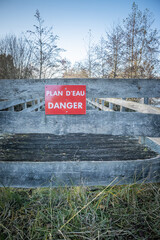 "Body of water, danger" French sign on the wooden fence of a bridge