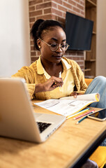 Fototapeta premium Young African American female student studying at home using laptop.